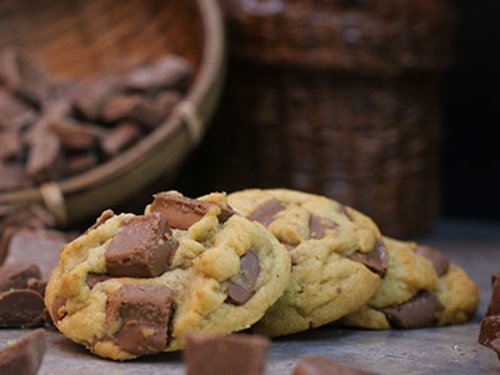 Soft-baked cookies loaded with chunks of chocolate, resting against a woven basket of chocolate pieces