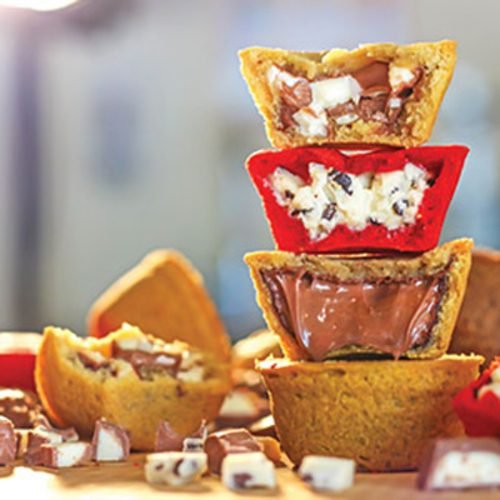 A stack of Camel Cookies cookie cups split open to show white chocolate, red velvet and molten chocolate fillings, with chopped chocolate pieces around the base
