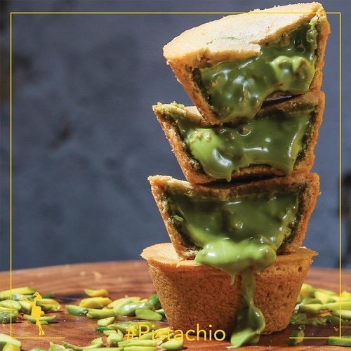 A stack of Camel Cookies pistachio cookie cups on a wooden board, molten pistachio cream spilling over the edges, with slivered pistachios scattered below