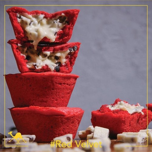 Bright red velvet cookie cups stacked in a column, the top two broken open to show a white chocolate filling flecked with dark cookie crumb